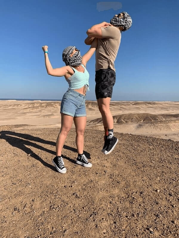 A girl lifting a guy with one arm in the desert